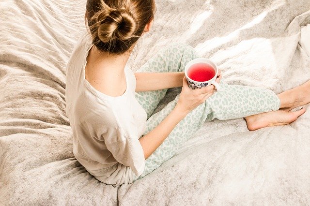žena sedící na posteli s šálkem čaje